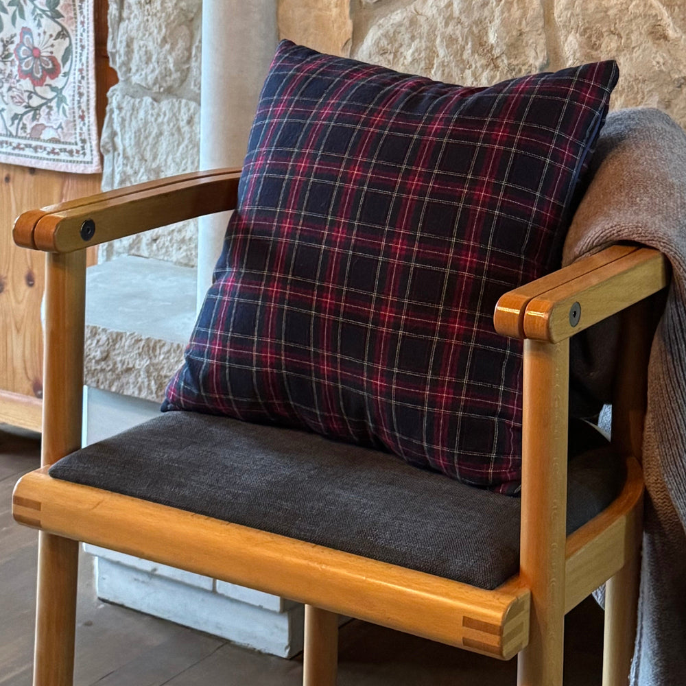 Wooden chair with plaid cushion and gray coverlet against a stone wall.