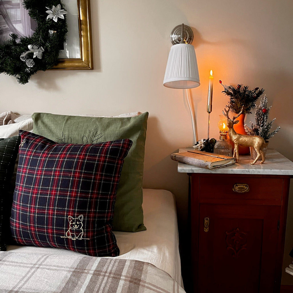 Decorative pillows on a bed with a nightstand featuring a lamp and small plant.