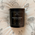 Black candle container labeled 'Drawing Room' on a floral-patterned background