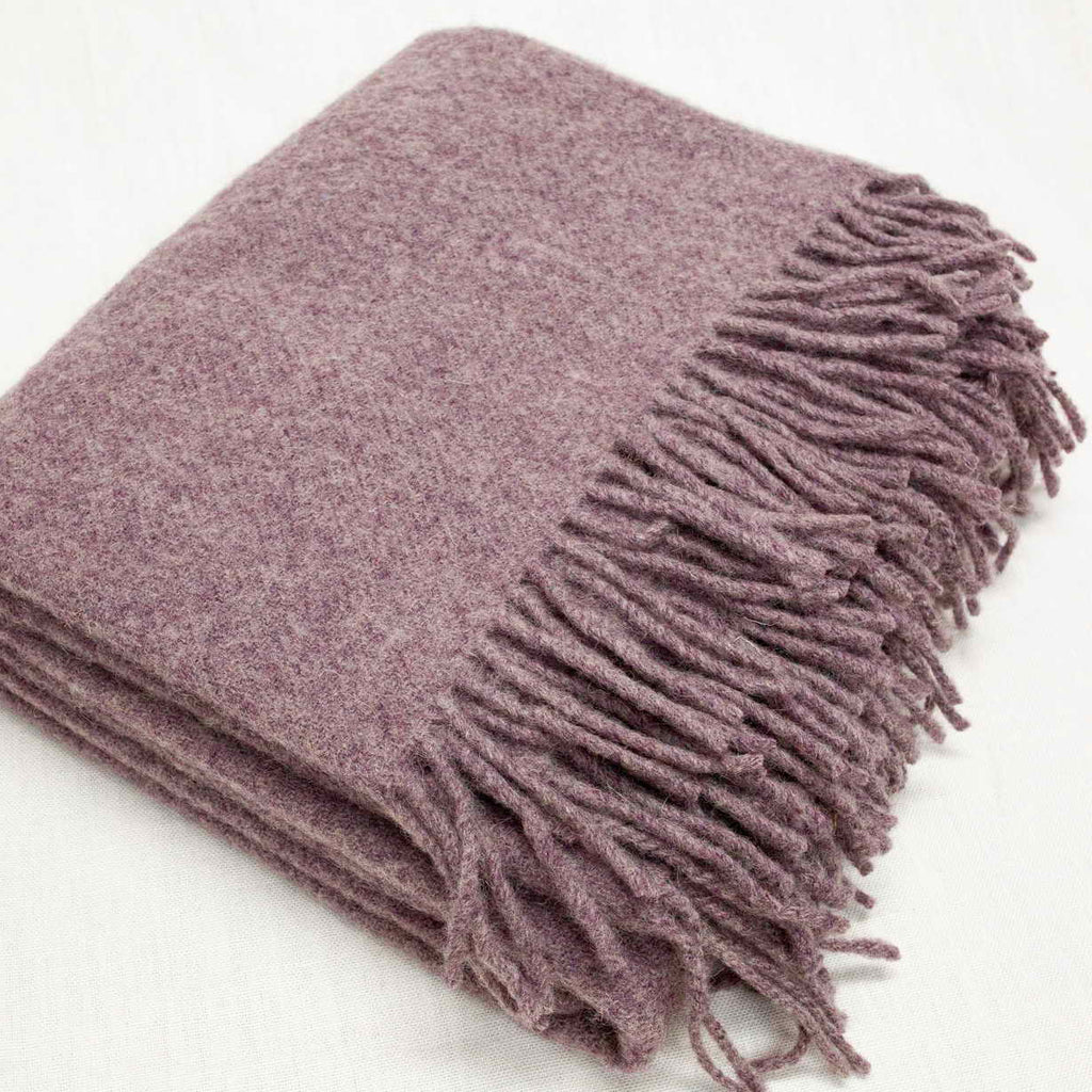 Folded lilac merino wool blanket with fringes on a white background