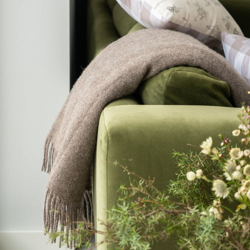 Green sofa with a brown blanket and decorative pillows against a neutral wall.